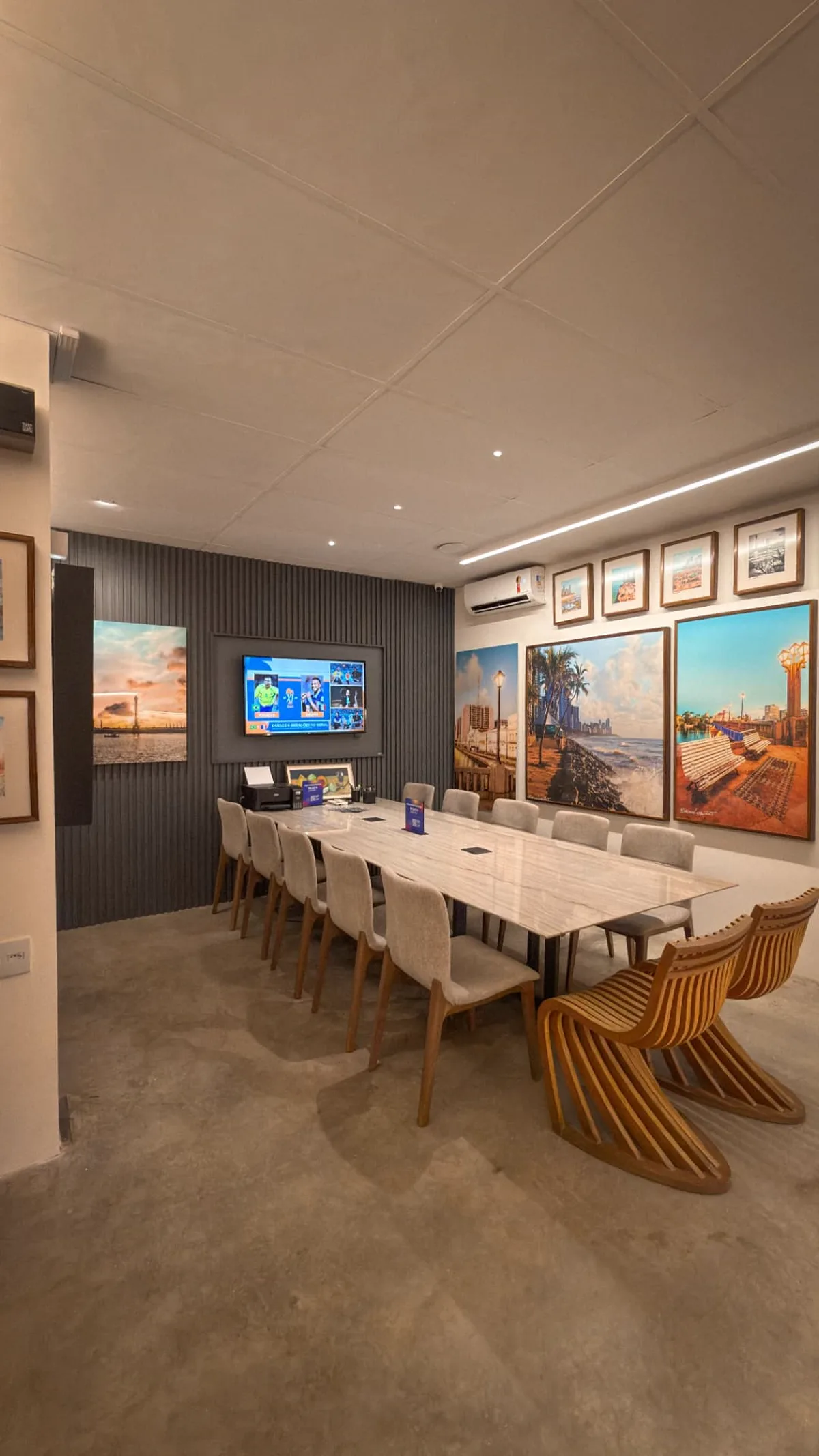 Sala de reunião da Casa Bruno Lima com mesa de mármore, cadeiras ripadas e TV